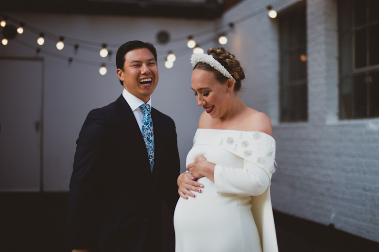 Groom and bride laughing, bride looking at her bump at the Bistrotheque, East London Wedding