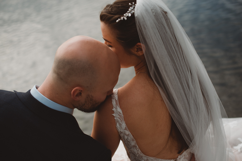 Intimate Outdoor Wedding by the river - bride and groom kiss on the shoulder, sitting by the river - Berkshire - relaxed wedding photography