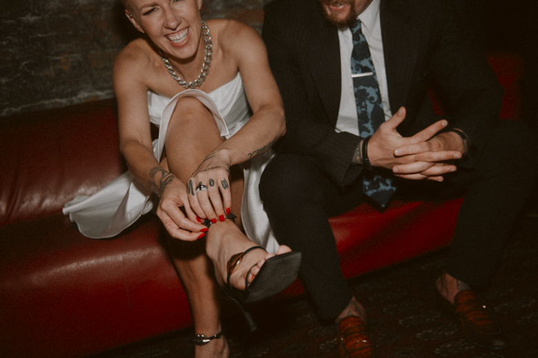 London Photographer Candid Style - Couple laughing, bride putting her shoes on - designer wedding dress